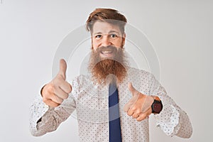 Young redhead irish businessman standing over isolated white background approving doing positive gesture with hand, thumbs up