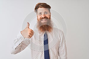 Young redhead irish businessman standing over isolated white background doing happy thumbs up gesture with hand