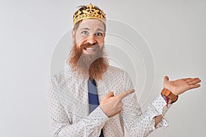 Young redhead irish businessman wearing crown king over isolated white background amazed and smiling to the camera while