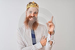 Young redhead irish businessman wearing crown king over isolated white background with a big smile on face, pointing with hand and