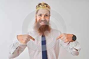 Young redhead irish businessman wearing crown king over isolated white background looking confident with smile on face, pointing