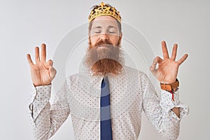 Young redhead irish businessman wearing crown king over isolated white background relax and smiling with eyes closed doing