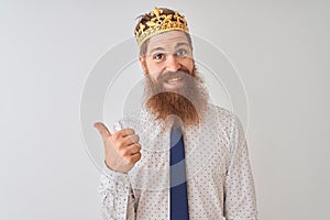 Young redhead irish businessman wearing crown king over isolated white background smiling with happy face looking and pointing to