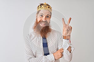 Young redhead irish businessman wearing crown king over isolated white background smiling with happy face winking at the camera