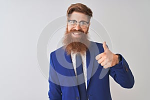 Young redhead irish businessman wearing suit and glasses over isolated white background doing happy thumbs up gesture with hand
