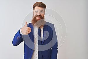 Young redhead irish businessman wearing suit standing over isolated white background doing happy thumbs up gesture with hand