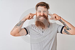 Young redhead irish man wearing grey polo standing over isolated white background covering ears with fingers with annoyed