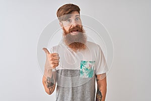 Young redhead irish man wearing t-shirt standing over isolated white background smiling with happy face looking and pointing to