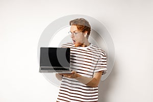 Young redhead man look impressed, showing laptop empty screen with logo banner. Guy in glasses checking out online
