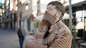 Young redhead man looking to the side with serious expression and arms crossed gesture at coffee shop terrace