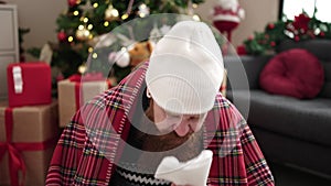 Young redhead man sitting on floor by christmas tree coughing at home