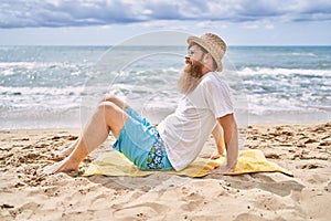 Young redhead man smiling happy sitting on the towel at the beach