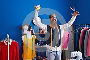 Young redhead man tailor smiling confident holding scissors and thread at clothing factory