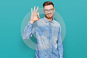 Young redhead man wearing casual denim shirt smiling positive doing ok sign with hand and fingers