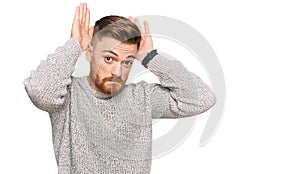 Young redhead man wearing casual winter sweater doing bunny ears gesture with hands palms looking cynical and skeptical