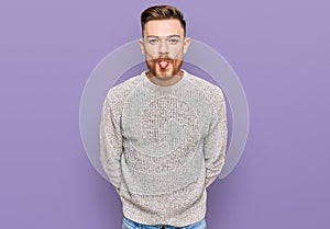 Young redhead man wearing casual winter sweater sticking tongue out happy with funny expression