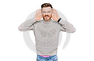 Young redhead man wearing casual winter sweater trying to hear both hands on ear gesture, curious for gossip