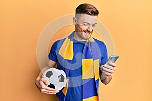 Young redhead man wearing hooligan scarf and using smartphone smiling with a happy and cool smile on face