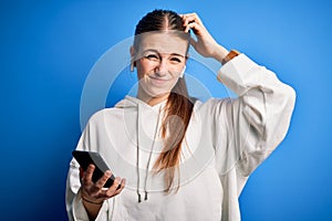 Young redhead sportswoman doing sport listening to music using earphones and smartphone confuse and wondering about question