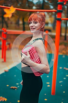 Young redhead sportswoman holding a foam roller in the park at vibrant autumn