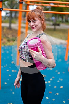 Young redhead sportswoman holding a foam and smiling roller in the park at autumn