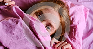 Young redhead Teenager Girl with blue eyes and red hairs Relaxing On pink Bed At Home closing her nose with pink sheet