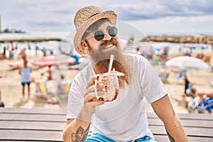 Young redhead tourist man drinking cocktail sitting on the bench at the beach