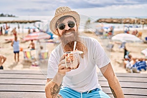 Young redhead tourist man drinking cocktail sitting on the bench at the beach