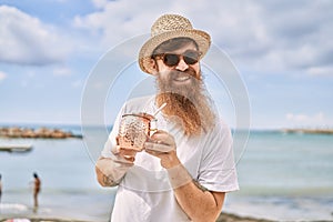 Young redhead tourist man smiling happy drinking cocktail at the beach