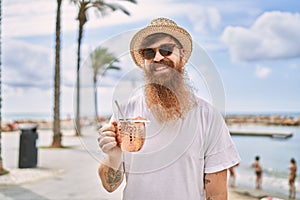 Young redhead tourist man smiling happy drinking cocktail at the beach