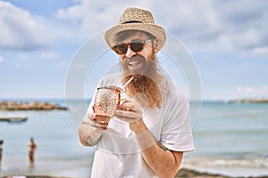 Young redhead tourist man smiling happy drinking cocktail at the beach