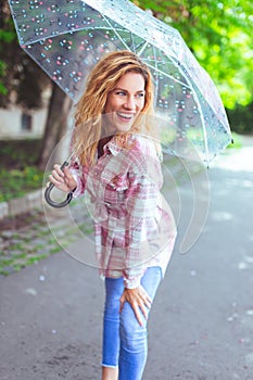 Young redhead urban woman with long wavy hair and transparent umbrella posing outdoors