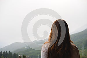 Young redhead woman admires mountains in autumn, back view.