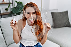 Young redhead woman doing coronavirus infection nasal test sticking tongue out happy with funny expression