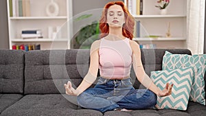 Young redhead woman doing yoga exercise sitting on sofa at home