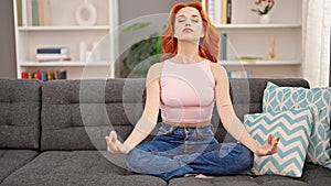 Young redhead woman doing yoga exercise sitting on sofa at home