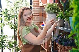 Young redhead woman florist smiling confident holding plant pot at flower shop