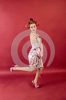 Young redhead woman with hair curlers dressed in neglige, peignoir, dressing gown posing on a burgundy background