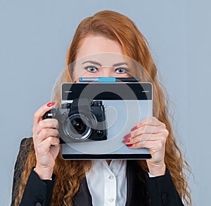 Young redhead woman holding a camera and a tablet.