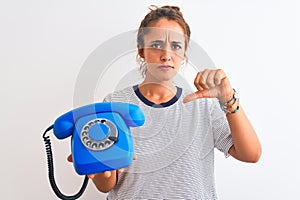 Young redhead woman holding classic retro telephone over isolated background with angry face, negative sign showing dislike with