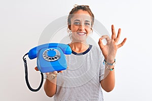 Young redhead woman holding classic retro telephone over isolated background doing ok sign with fingers, excellent symbol