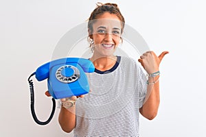 Young redhead woman holding classic retro telephone over isolated background pointing and showing with thumb up to the side with