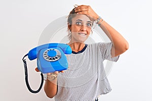 Young redhead woman holding classic retro telephone over isolated background stressed with hand on head, shocked with shame and