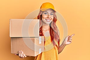 Young redhead woman holding delivery package smiling happy pointing with hand and finger to the side