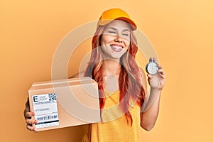 Young redhead woman holding delivery package and stopwatch smiling and laughing hard out loud because funny crazy joke