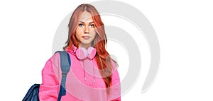 Young redhead woman holding student backpack and books thinking attitude and sober expression looking self confident