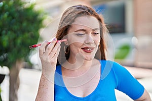 Young redhead woman miling confident listening audio message by the smartphone at street