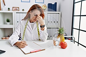 Young redhead woman nutritionist doctor at the clinic tired rubbing nose and eyes feeling fatigue and headache