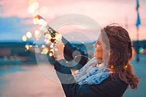 Young redhead woman playing with fairy lights outdoors