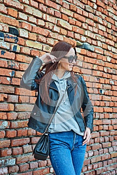 Young redhead woman posing near the brick wall